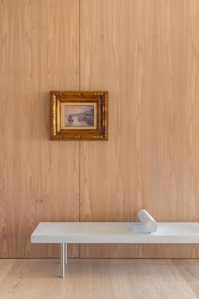 A minimalist interior design featuring a wooden frame with a framed painting and a modern, sleek bench with a cylindrical obj