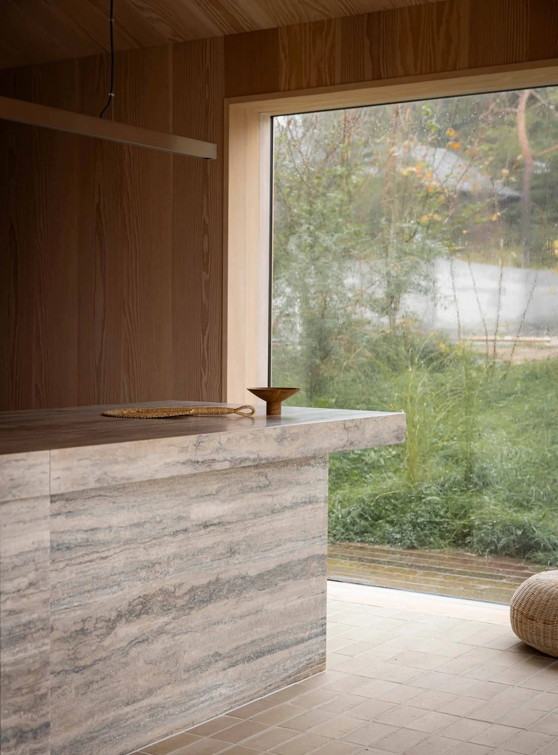 A modern interior design featuring a stone countertop with a woven rope decoration and a wooden bowl on top, framed by a larg