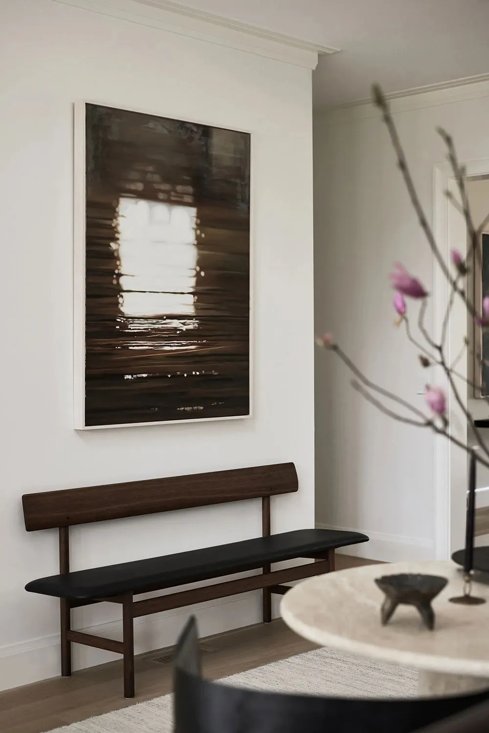 A minimalist living room features a wooden bench and a large framed artwork depicting a window reflected in water.