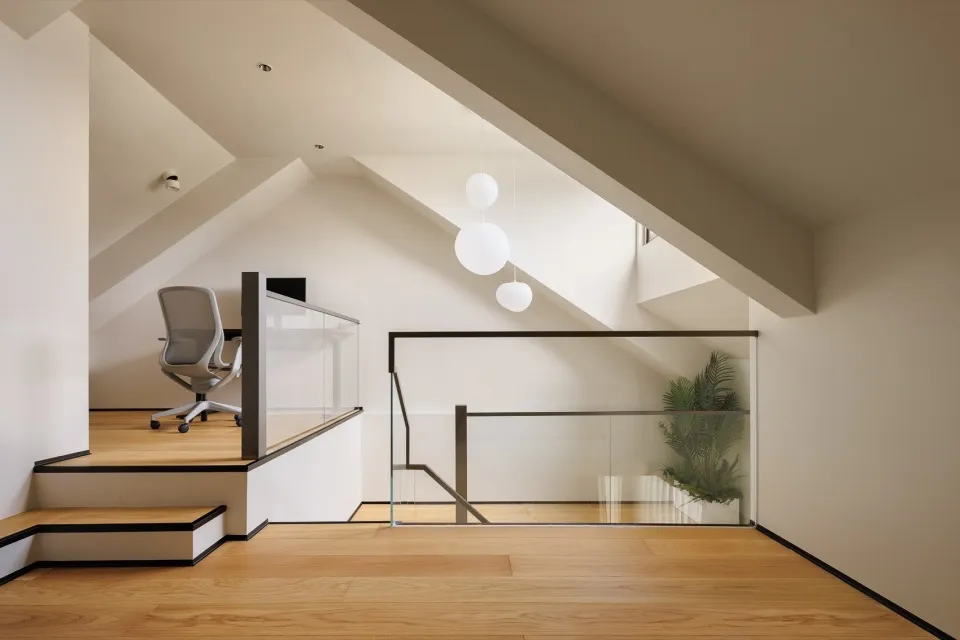 A modern home office with glass partitions, wooden floors, a white chair, and a hanging white light fixture.