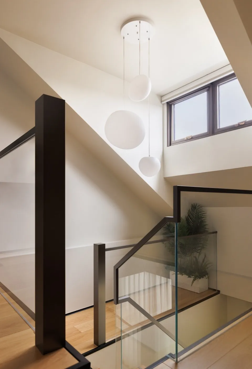 Modern interior with glass stair railing, steel accents, oak flooring, and a plant.