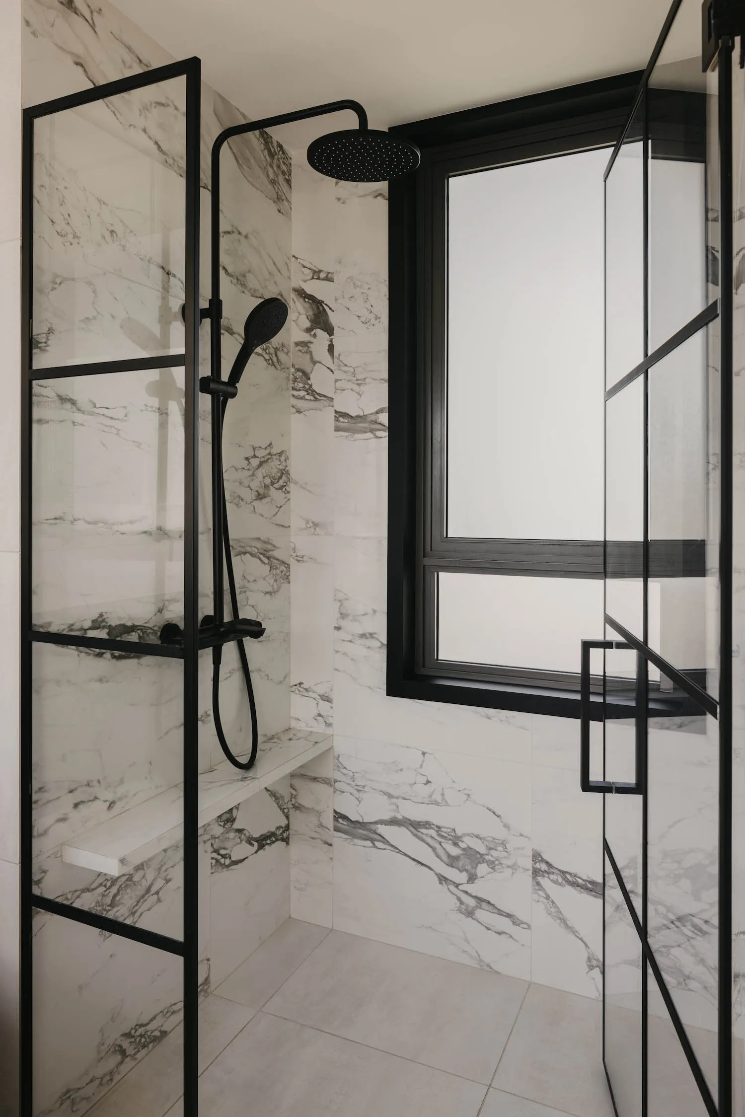 A minimalist bathroom with a marble shower area, black fixtures, and a window.