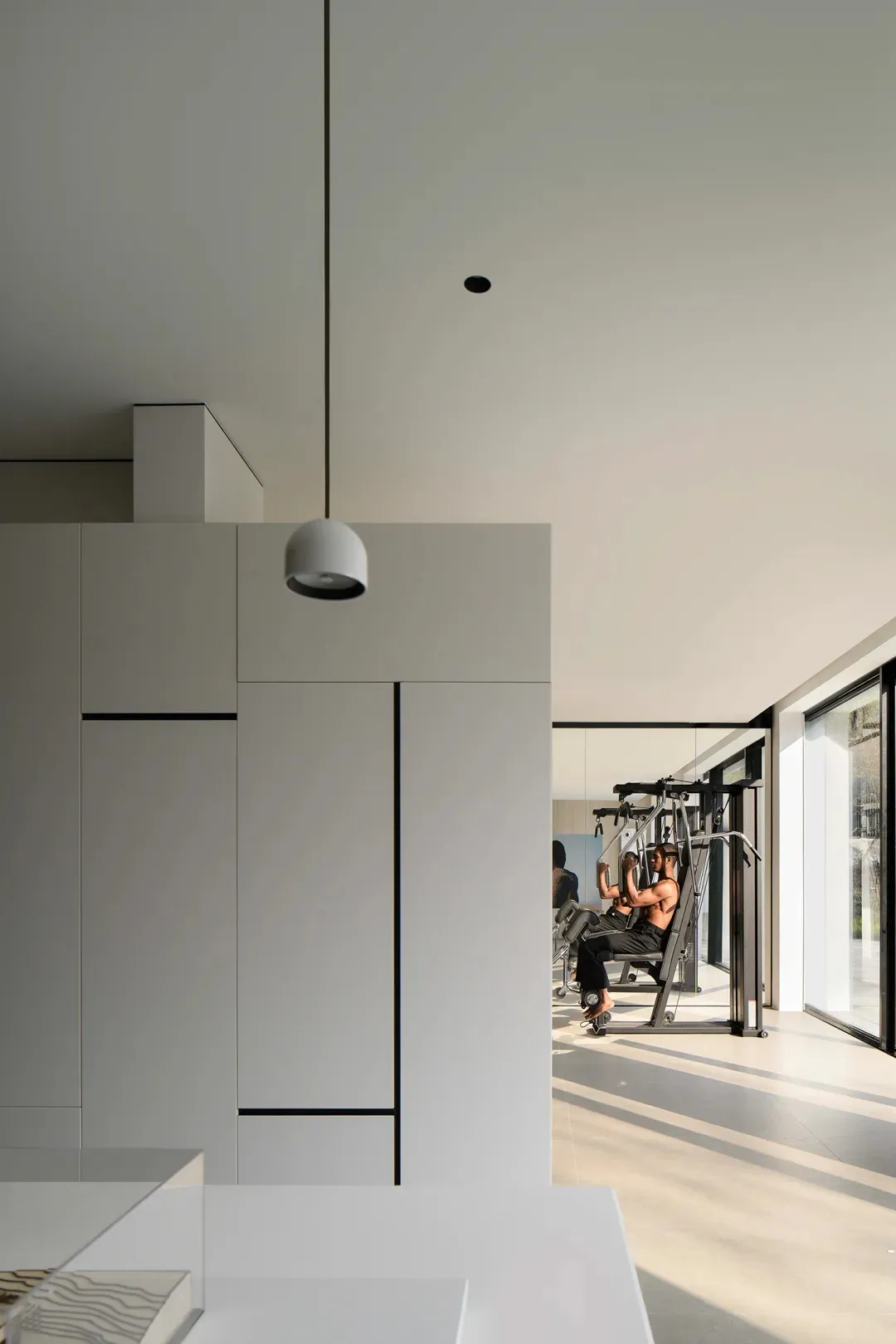 A minimalist home gym with concrete flooring and white cabinets, featuring a workout machine and a person exercising.