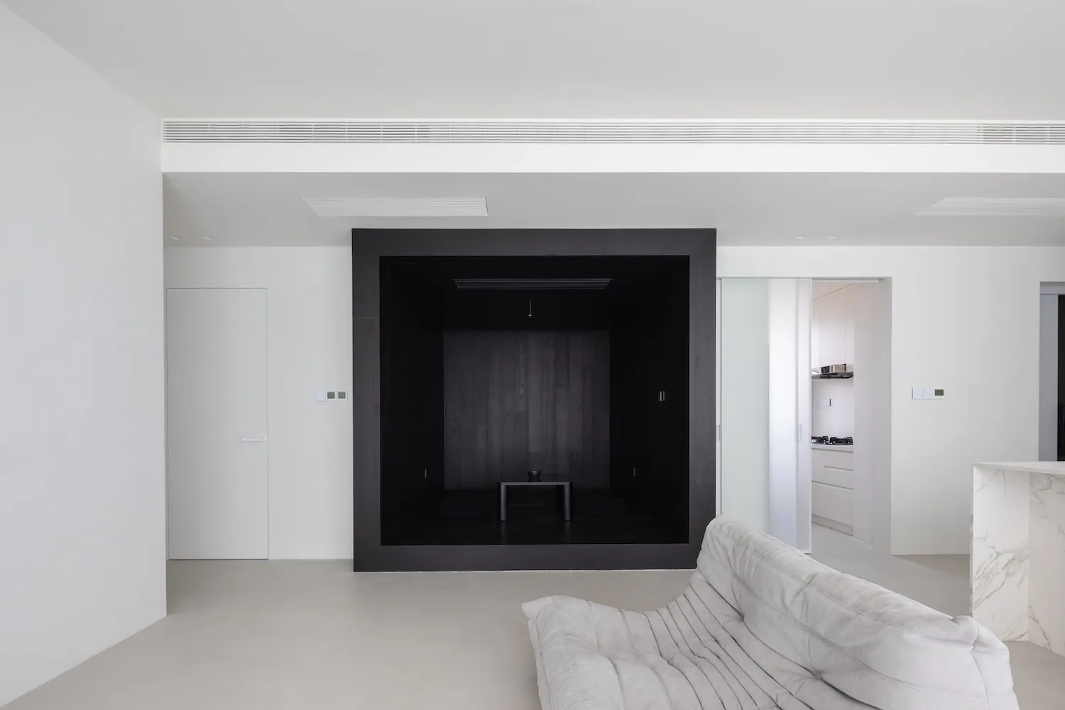 A modern minimalist living room with a black box feature wall, concrete floor, and white sofa.