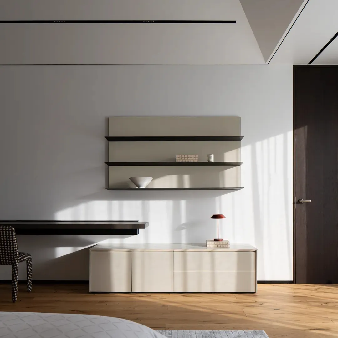 Minimalist bedroom featuring wood flooring and furniture, with a white wall and a floating shelf.