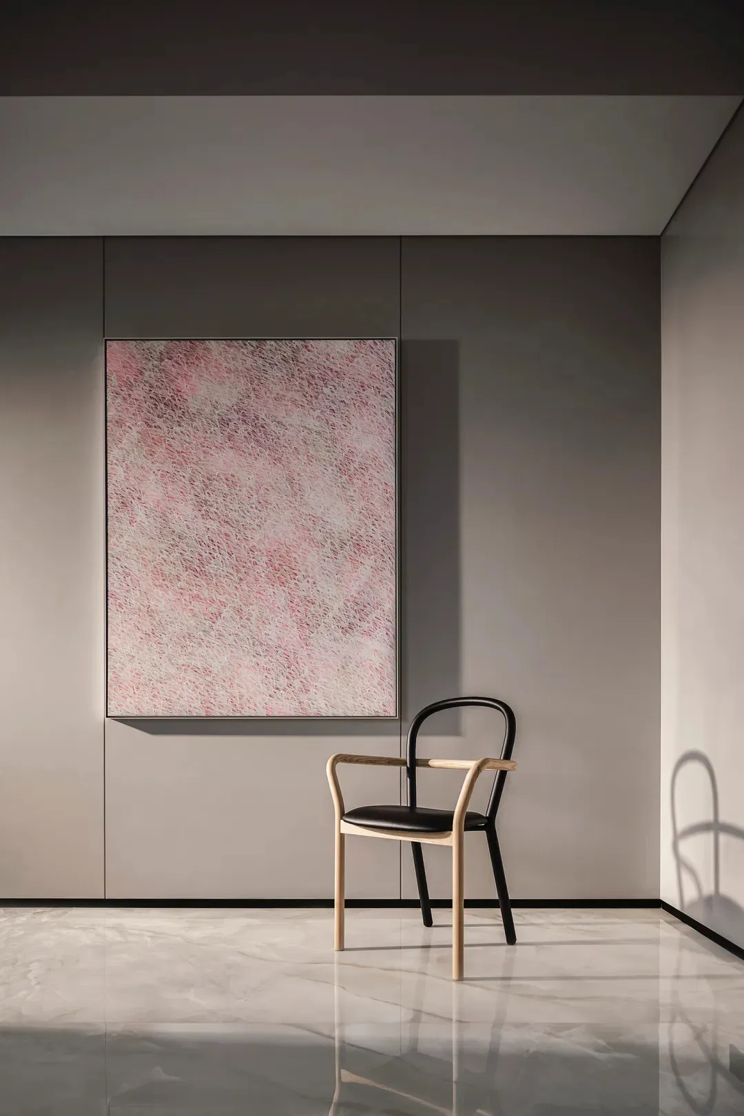 A minimalist black chair with wooden arms and a padded seat sits beside an abstract art wall in a modern interior design sett