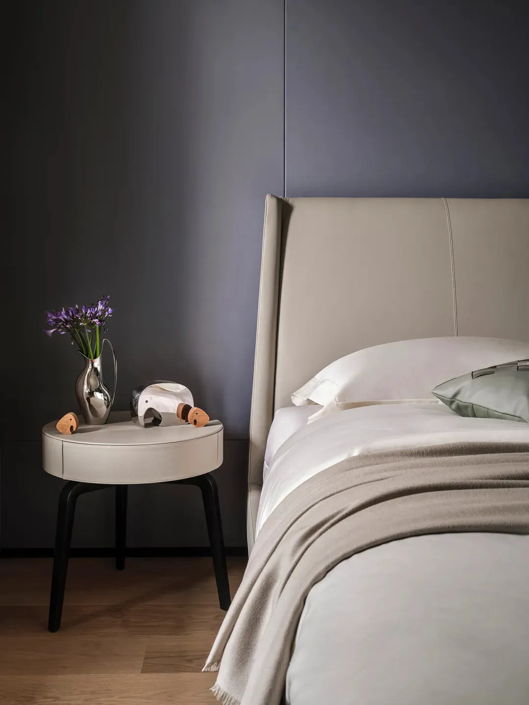 A minimalist bedroom featuring a bed with a beige leather headboard and fabric bedding.
