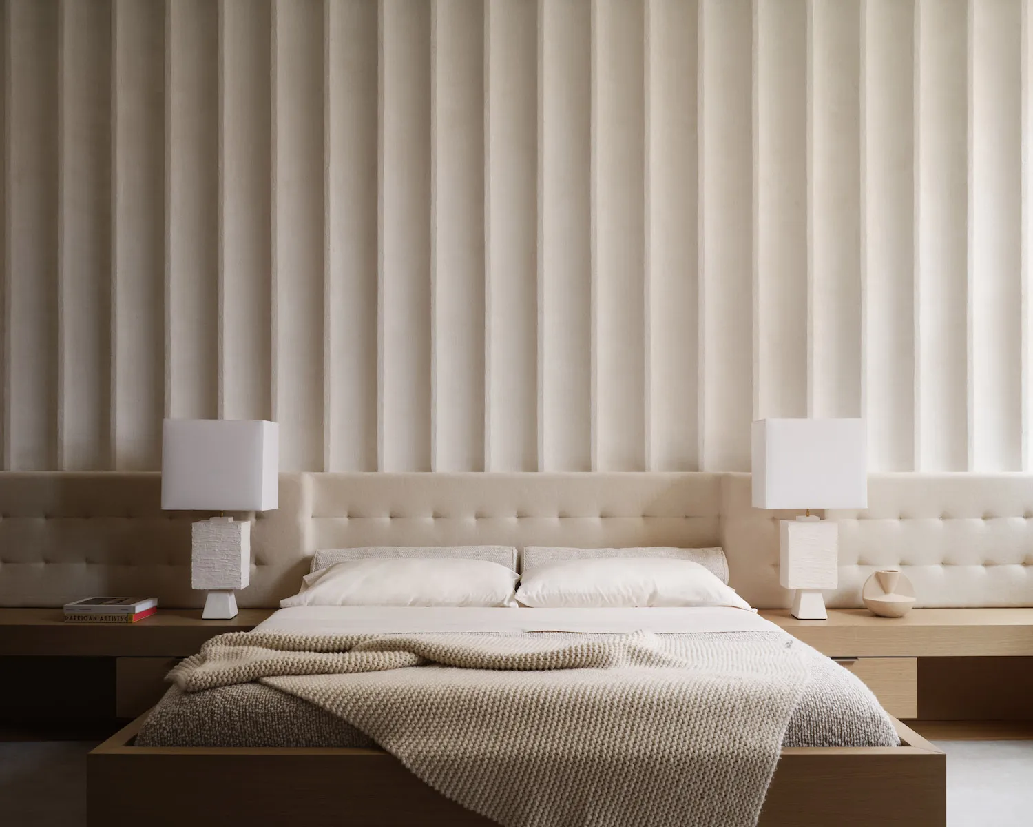 Minimalist bedroom with a white fabric bed and light-colored walls.