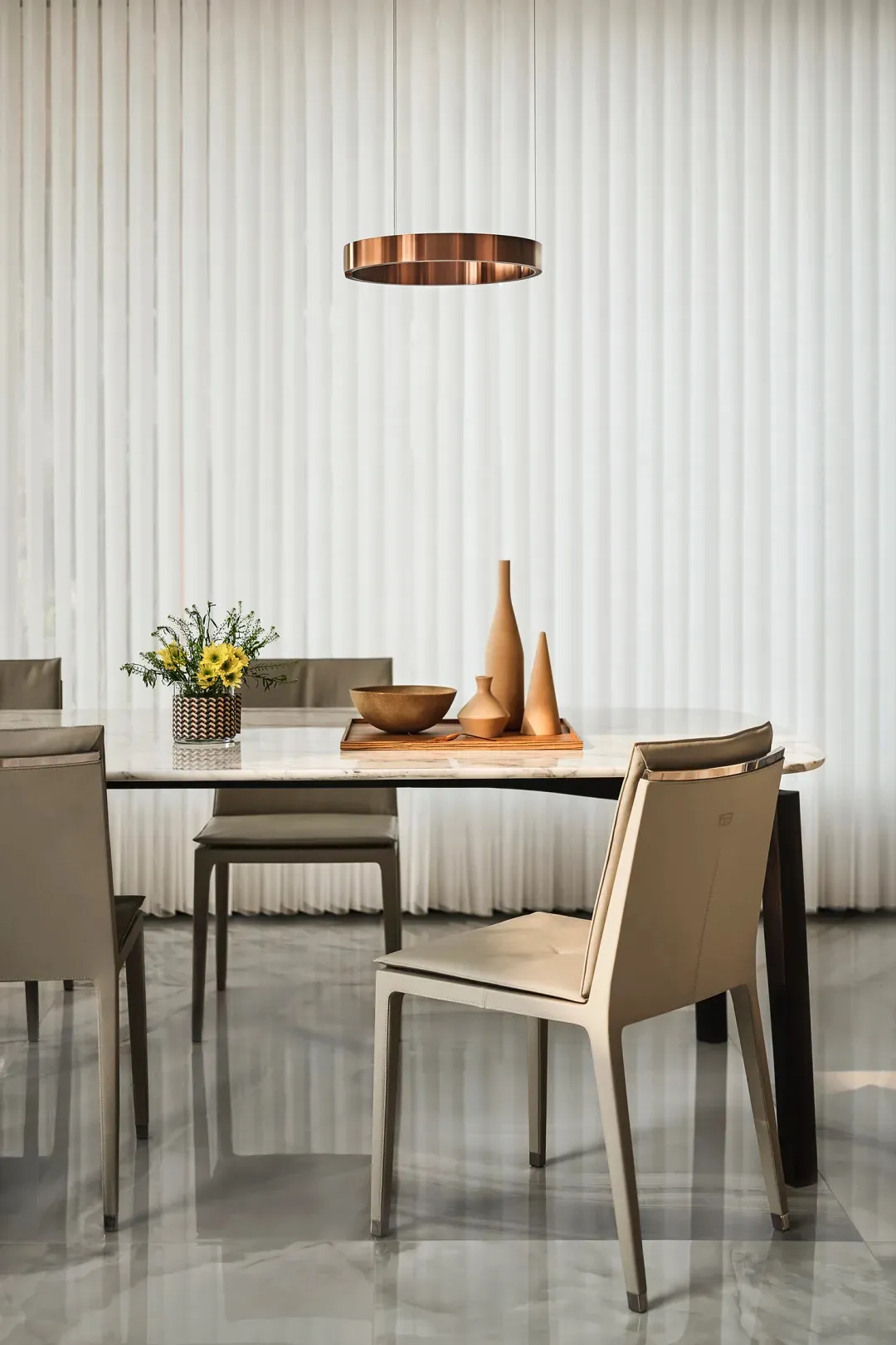 Modern dining room featuring a marble table with minimalist chairs, vase, and tray arrangement.