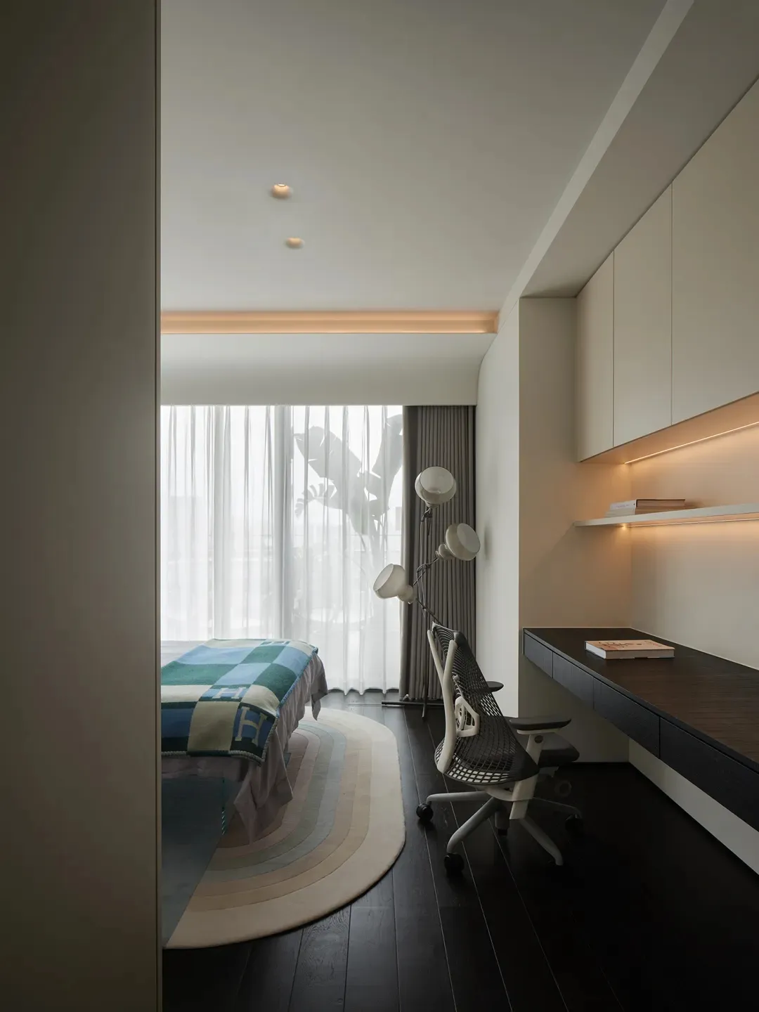 Modern minimalist bedroom with neutral tones, featuring a bed covered in blue and green checkered bedding and a sleek, ergono