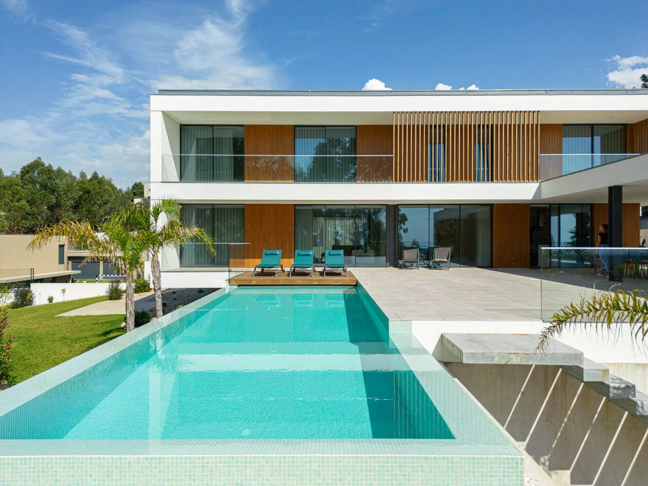 Modern minimalist pool house exterior with white facade, large windows, wooden accents, and a rectangular swimming pool.