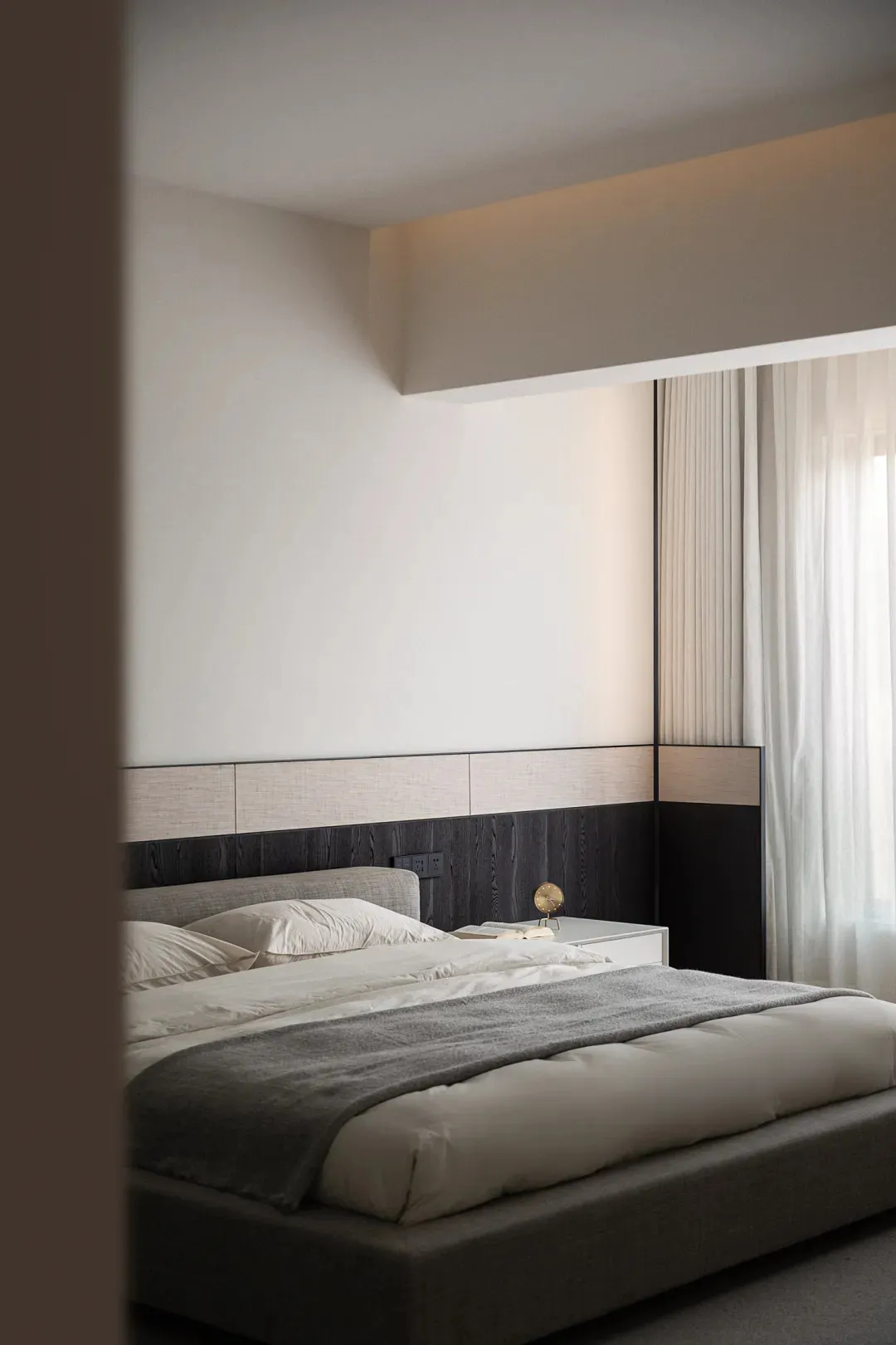 A modern minimalist bedroom with a fabric bed, white walls, and curtains.