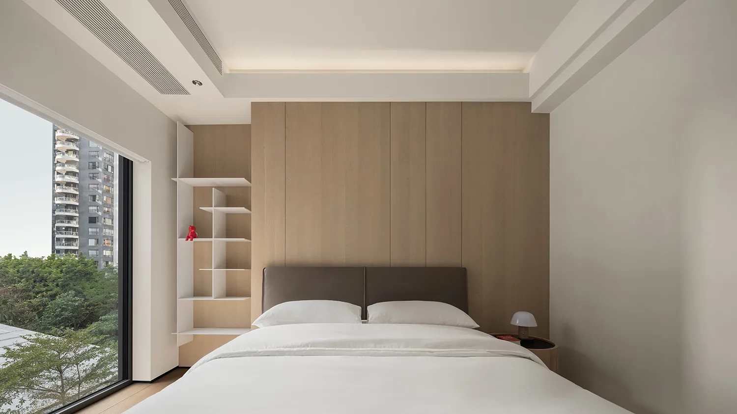 A minimalist bedroom featuring wood-paneled walls, a white bed with light-colored bedding, and a modern, open shelving unit.