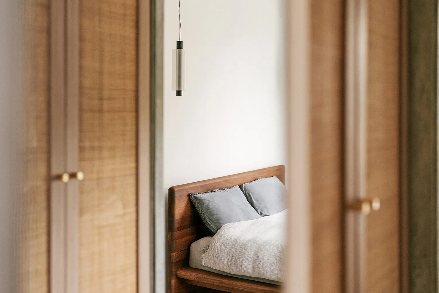 Modern minimalist bedroom featuring a wooden bed with white bedding and pillows, minimalistic design, and a hanging lamp.
