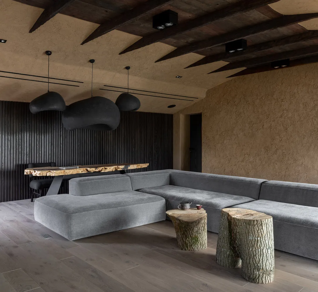 A modern living room featuring a concrete wall, a large corner sofa, and wooden tree stump tables.