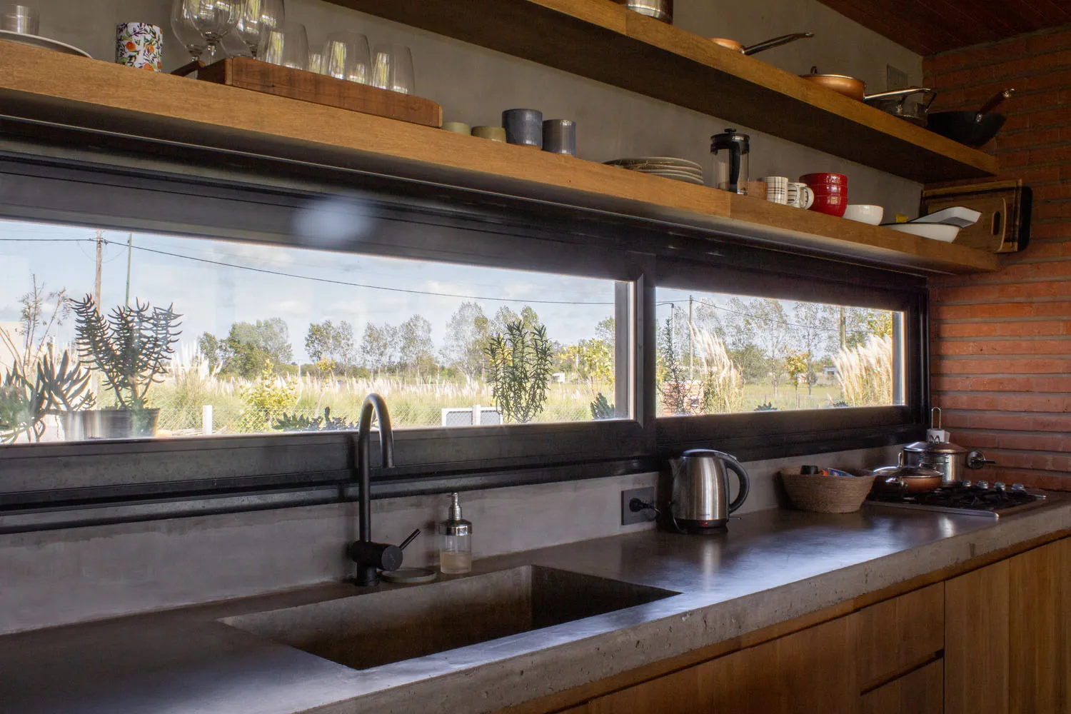 A modern, minimalist kitchen with concrete countertops and backsplash, featuring a large window and a double sink.
