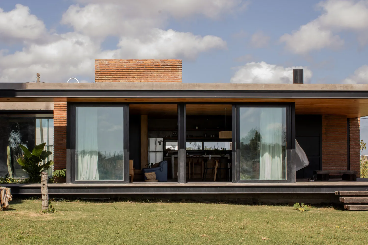 A modern house with large windows, brick exterior, concrete roof, and glass panels on the ground level.