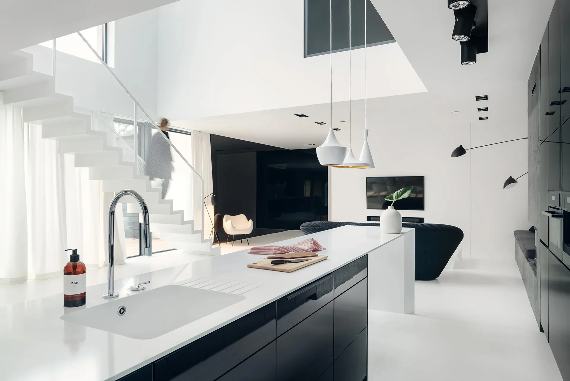A modern minimalist white kitchen with a sleek island counter, stainless steel sink, and pendant lights.