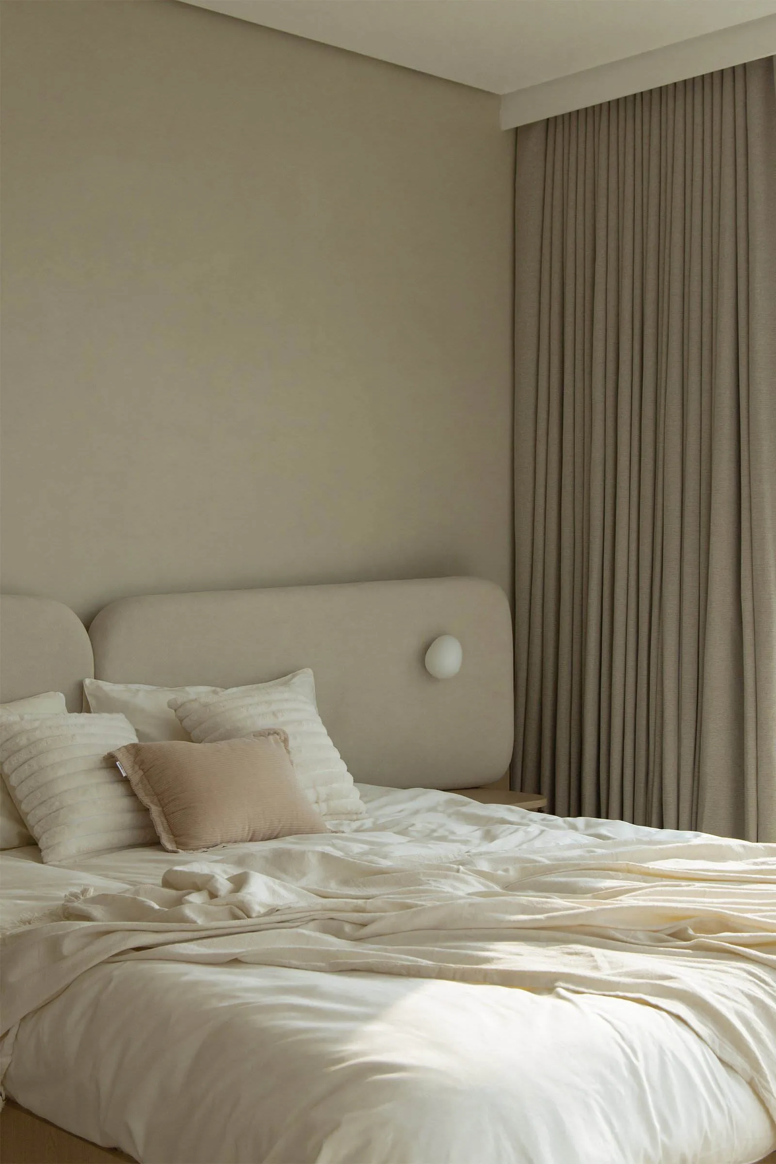 A minimalist bedroom with a bed dressed in neutral colors, including white sheets, a beige throw pillow, and a beige headboar