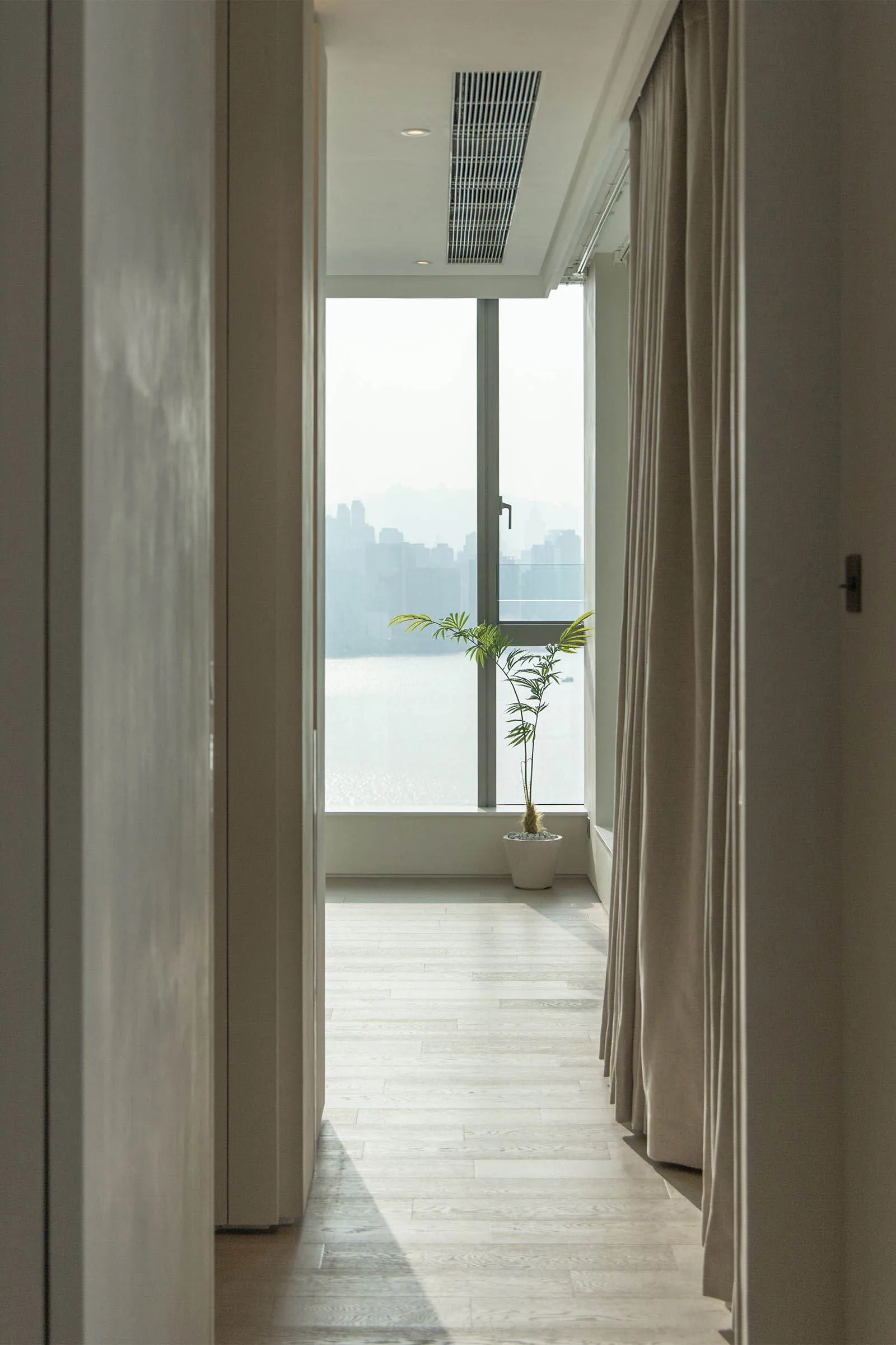 A modern residential hallway featuring white oak wood flooring and a view through the window to the cityscape.
