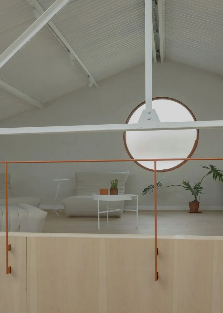 A minimalist living space featuring wood flooring, white furniture, and a circular window.