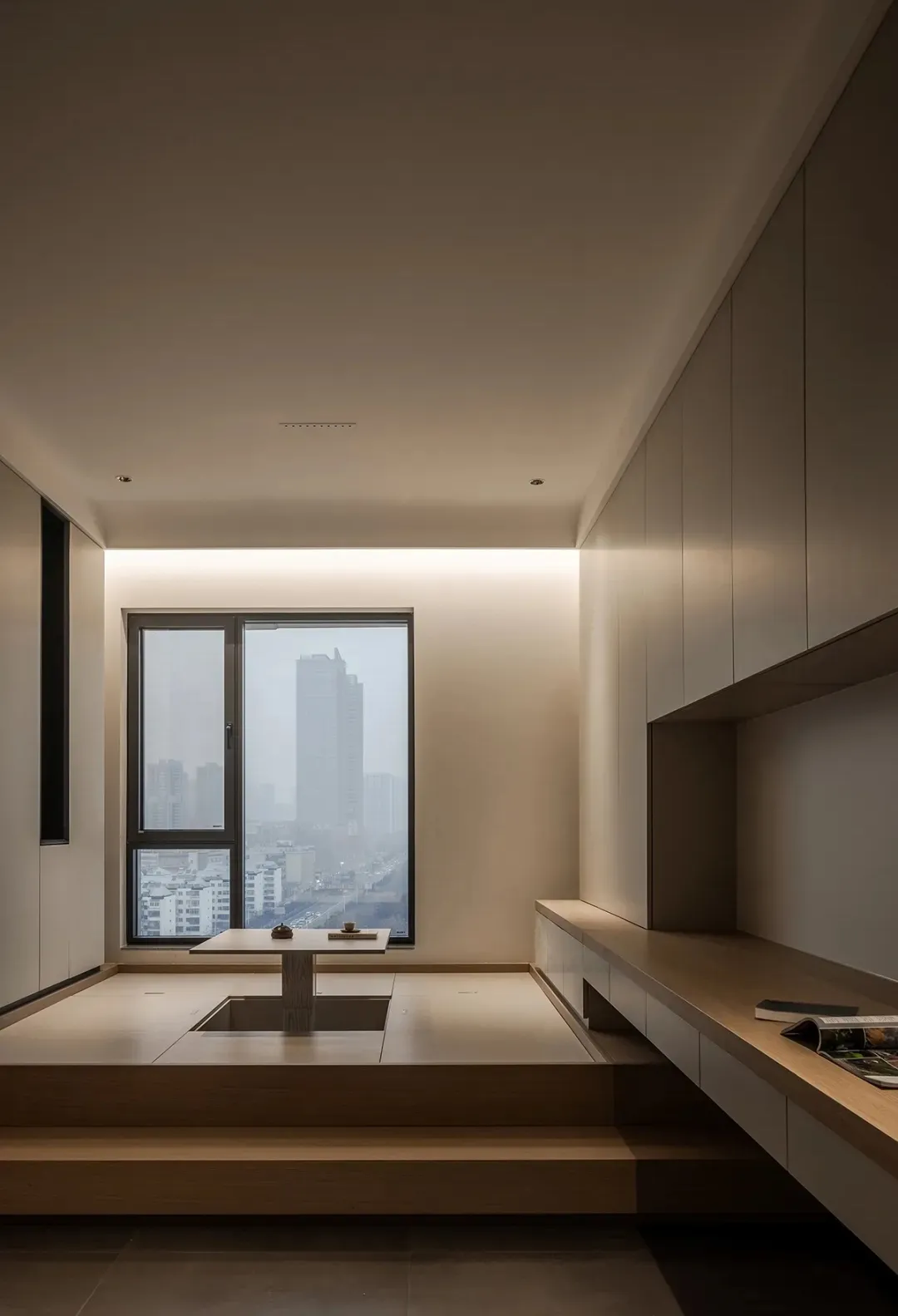 Modern living room with wooden accents, featuring a low table and steps leading to a window overlooking a cityscape.