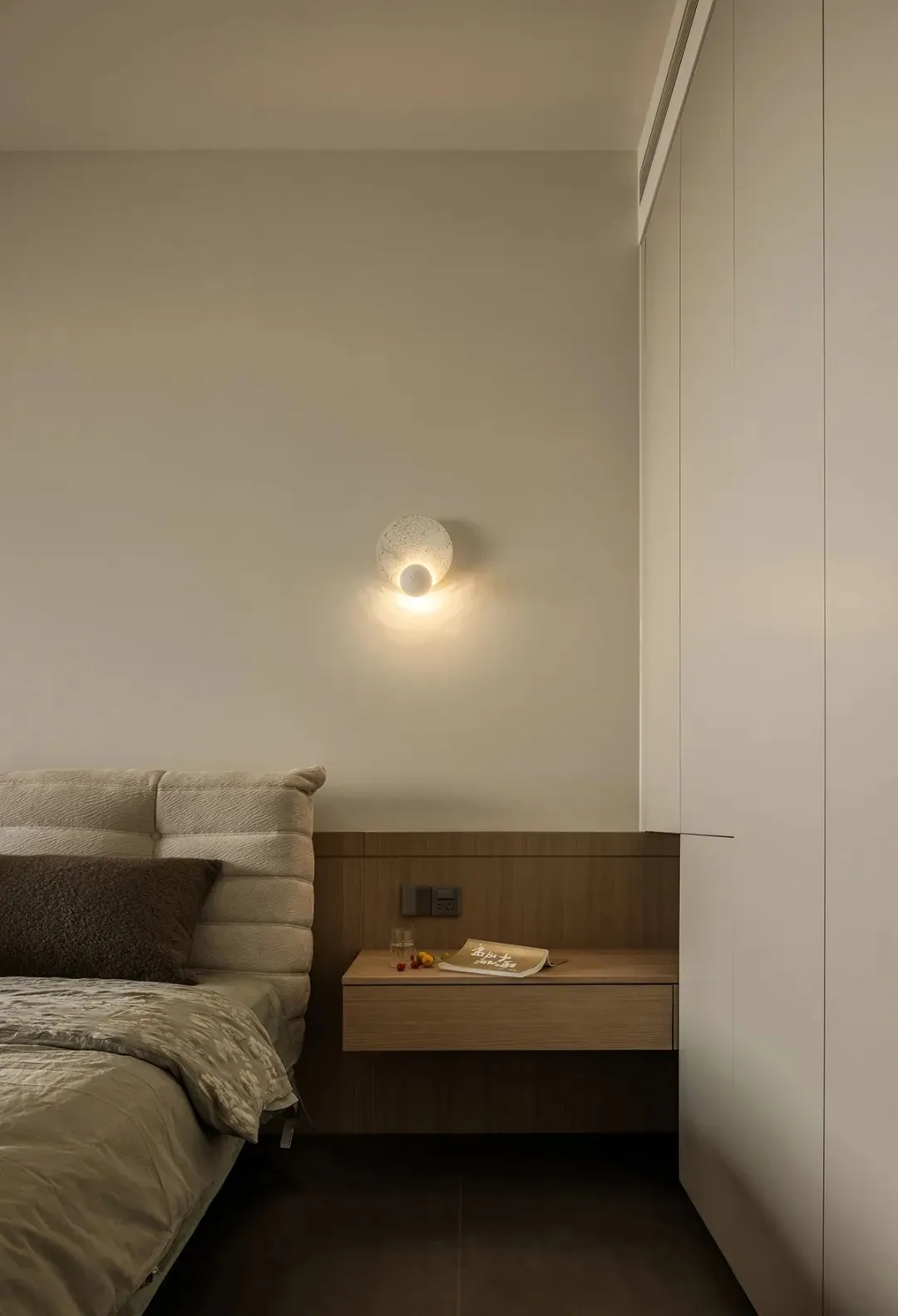 A modern minimalist bedroom with a single bed adorned with a beige textured headboard and matching cover, accompanied by a fl