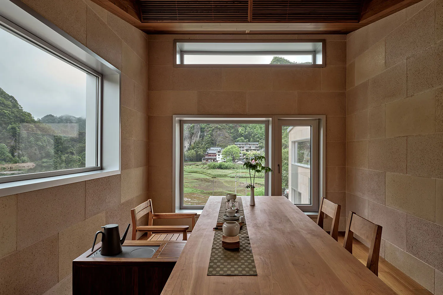 Modern minimalist dining room with a wooden table and large windows overlooking a scenic landscape.