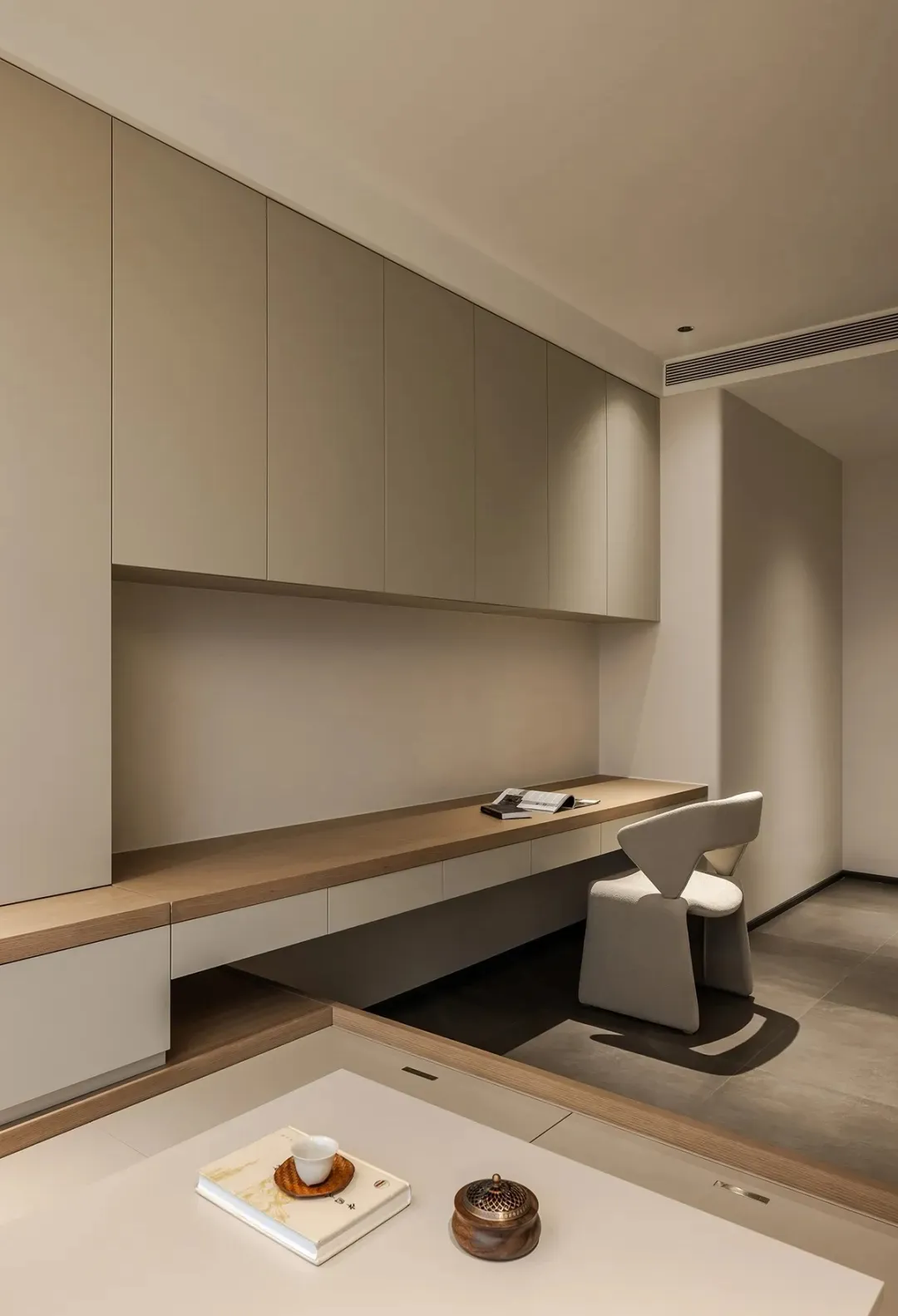 A minimalist home office featuring concrete and wooden surfaces with a sleek desk and modern chair