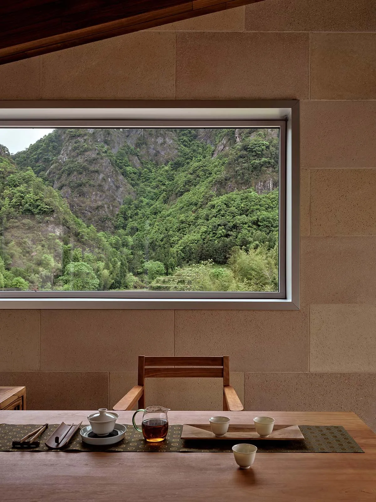 A minimalist tea room featuring a wooden table set with traditional tea utensils, surrounded by a natural stone wall and fram