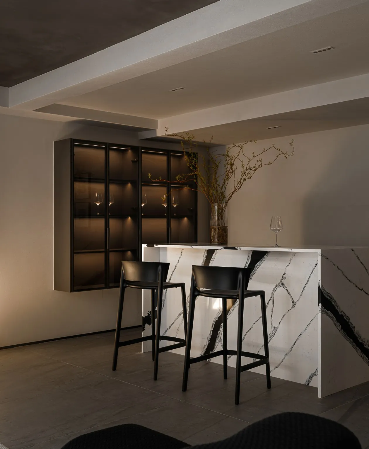 A minimalist bar seating area with marble countertops and black stools.