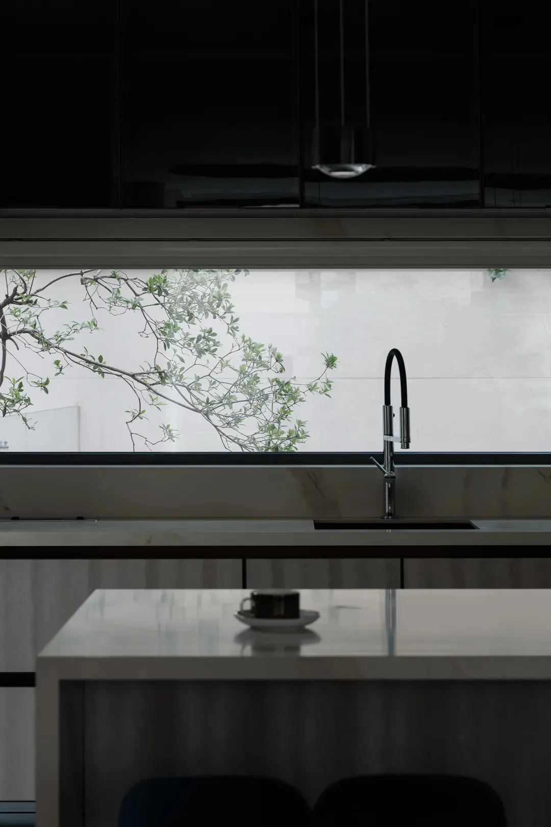 A modern, minimalist kitchen with a marble countertop and a view of greenery outside the window.