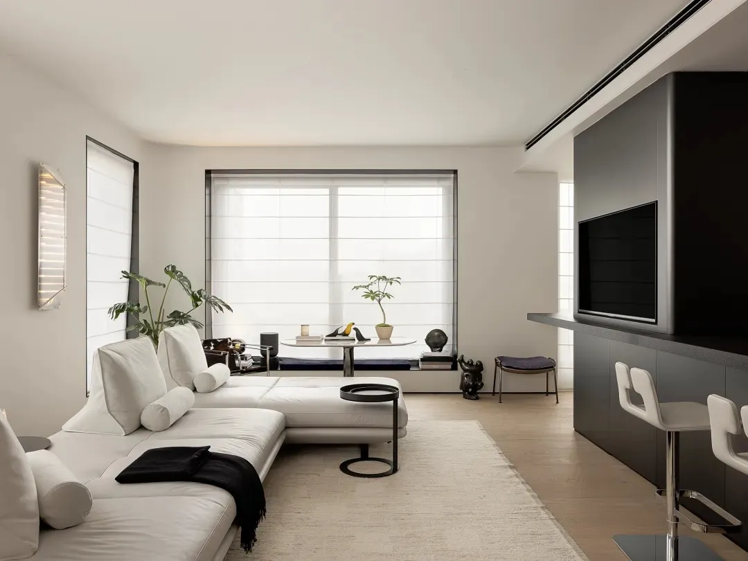 A minimalist, modern living room with a white leather sofa, wood flooring, and a large window.