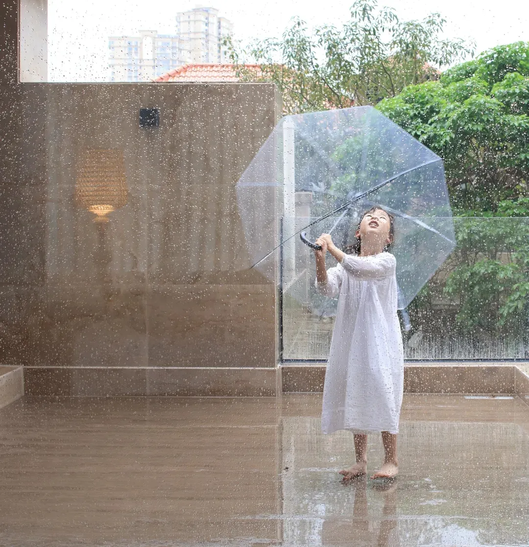A child holding a clear umbrella in the rain, standing on a wet, reflective surface.