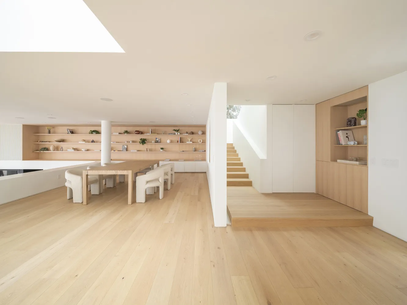 A modern residential entryway featuring white wooden floors, minimalist design, and a combination of white and beige elements
