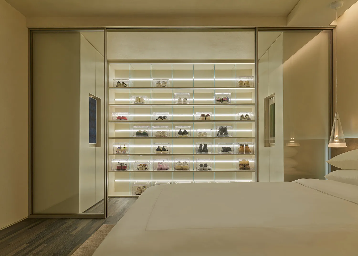 A sleek, minimalist bedroom features a glass-enclosed shoe collection displayed on shelves.