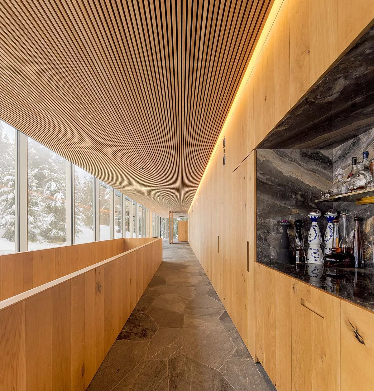 Modern interior corridor with wooden walls and ceiling, featuring a bar area with black marble countertops and assorted bottl