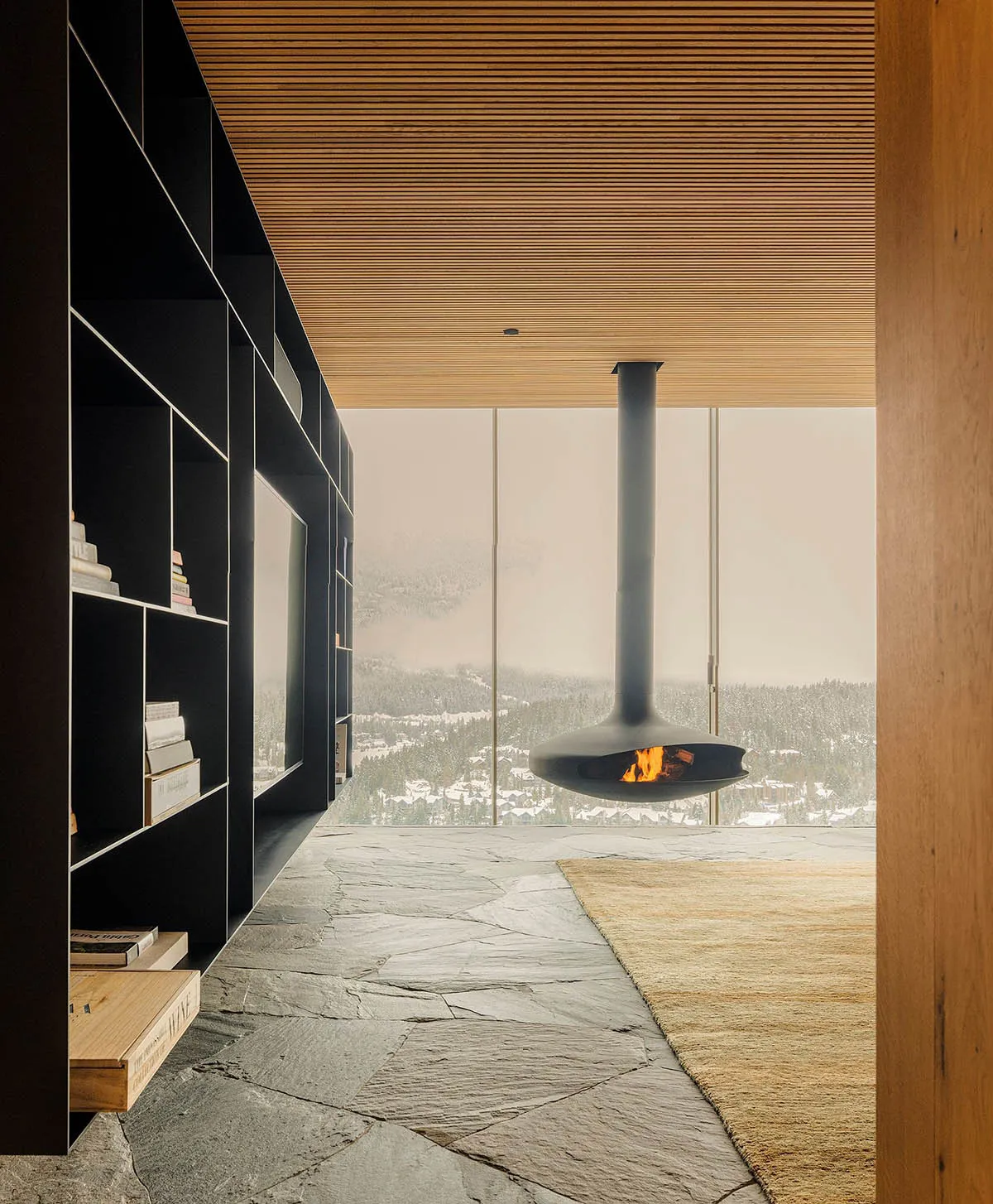 Modern minimalist living room with suspended fireplace and floor-to-ceiling windows overlooking snowy landscape.