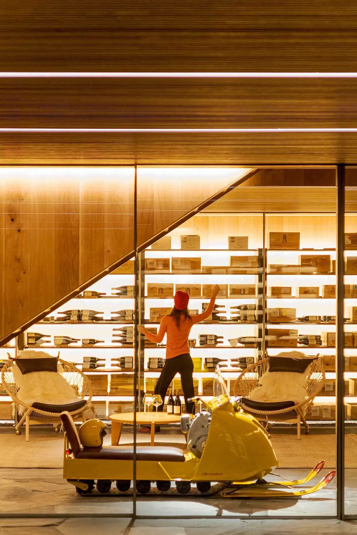 A modern wine bar featuring a wooden interior with illuminated shelves displaying bottles of wine and a yellow snowmobile in