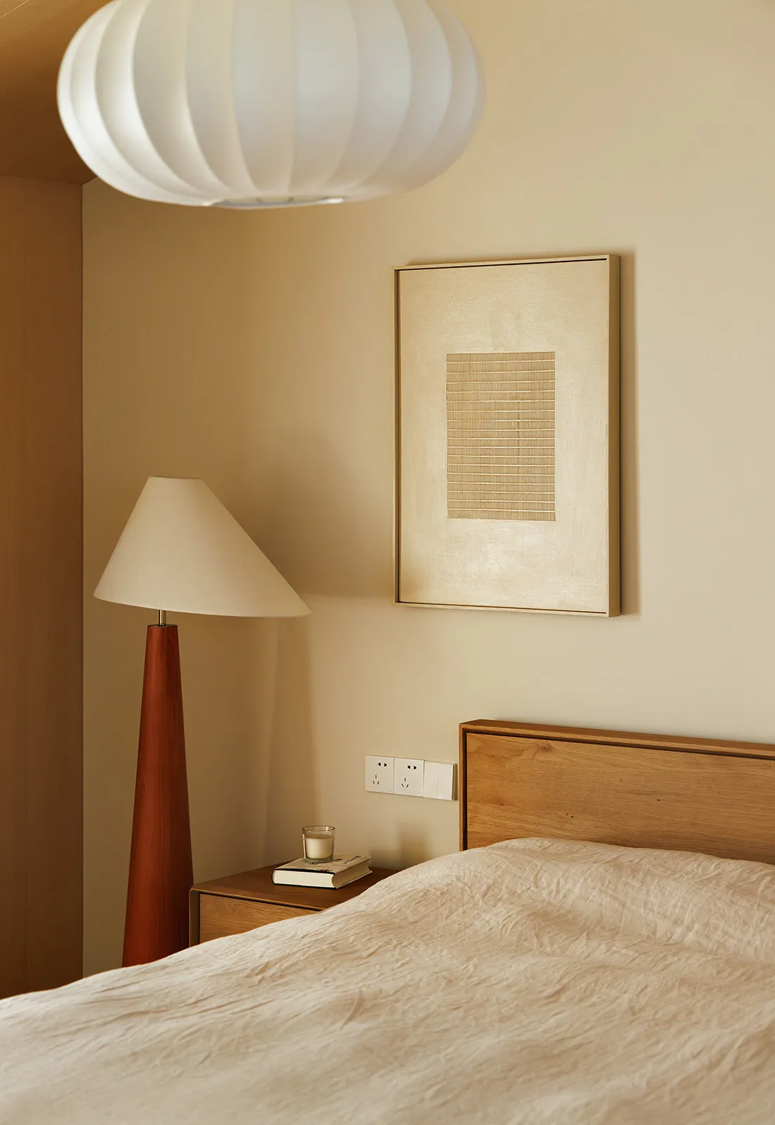 A serene minimalist bedroom featuring a wooden headboard and textured bedding, with a floor lamp and a wall-mounted artwork.