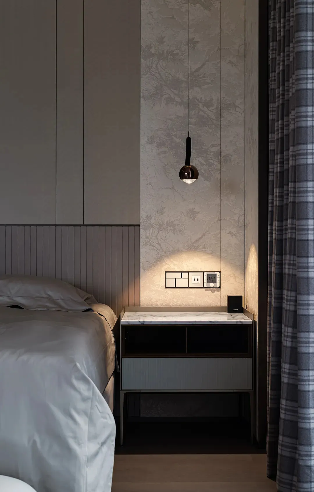 Minimalist bedroom with a modern upholstered headboard on a bed frame, illuminated by a hanging lamp, and a nightstand with a