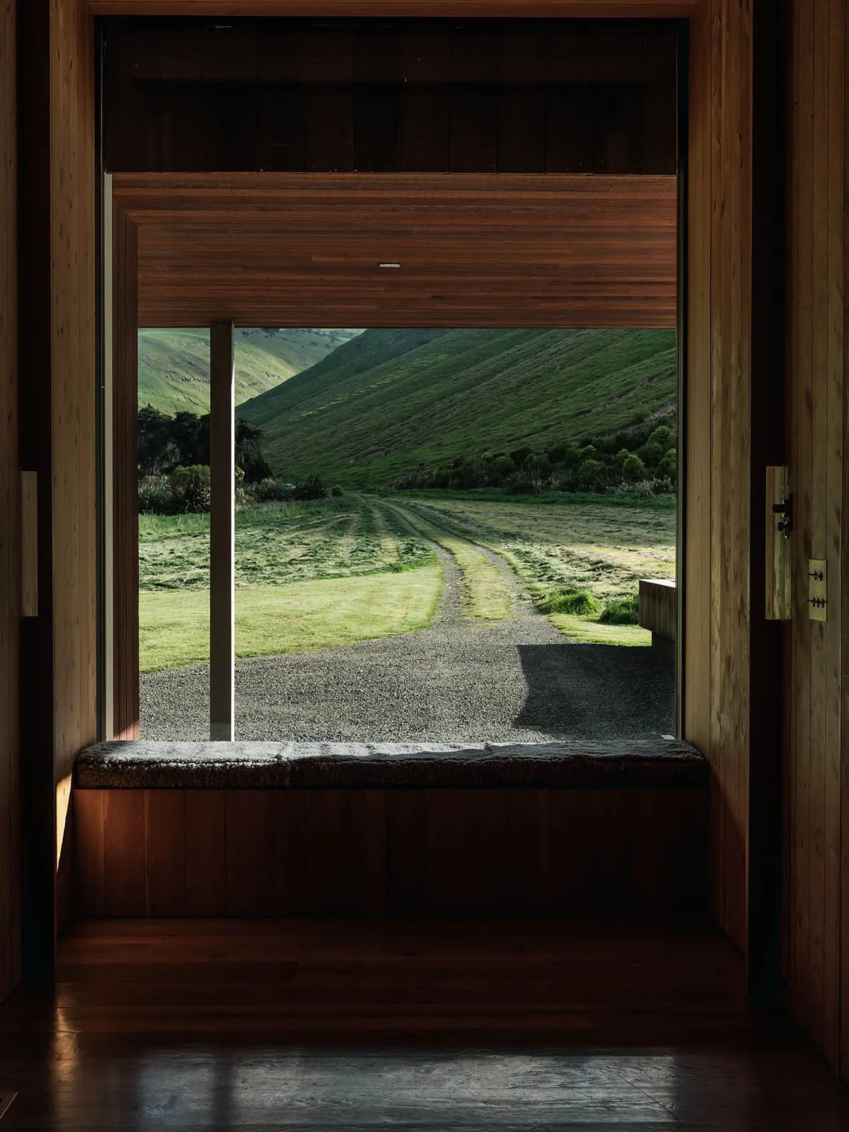 A view from the interior of a wooden building looking out through a window onto a rural road and hills.