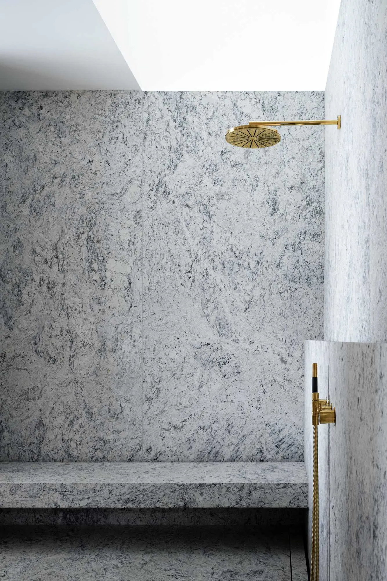 A minimalist bathroom featuring granite walls and a brass shower head