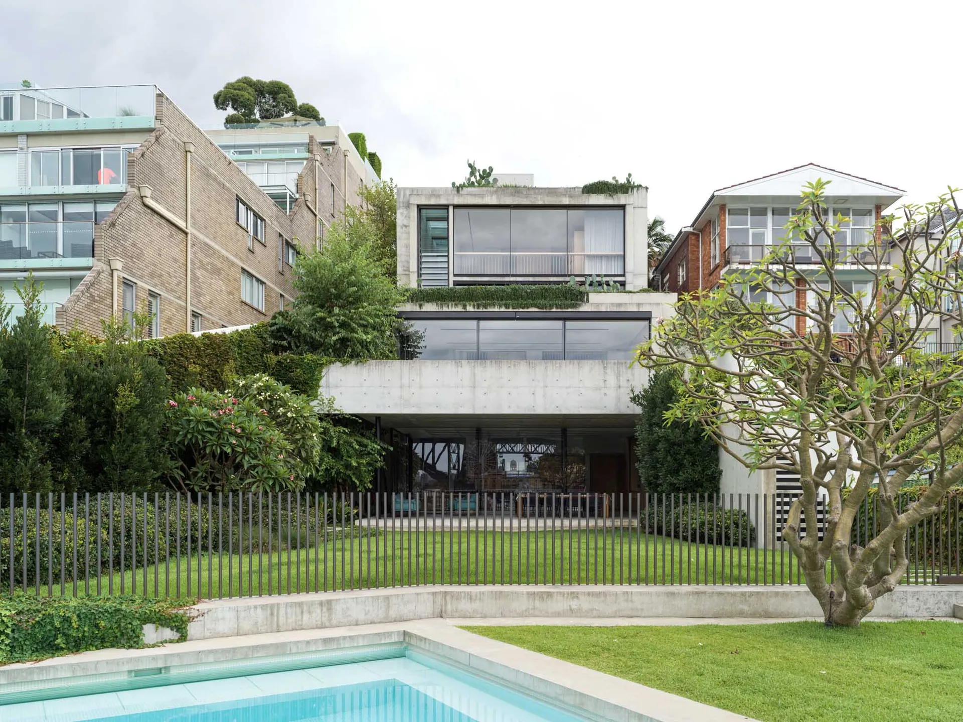 A modern residential home exterior showcasing a concrete facade with large glass windows and a rooftop garden.