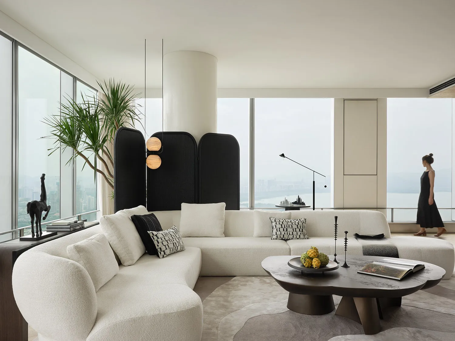 Modern living room with a white fabric couch, minimalistic design, and large windows overlooking a cityscape.