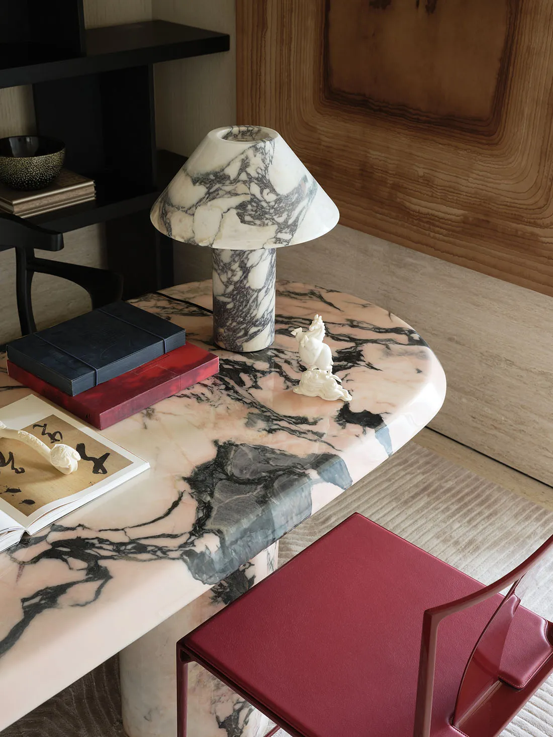 A modern office desk featuring a round, light pink and white marble top, accompanied by a black chair and various decorative