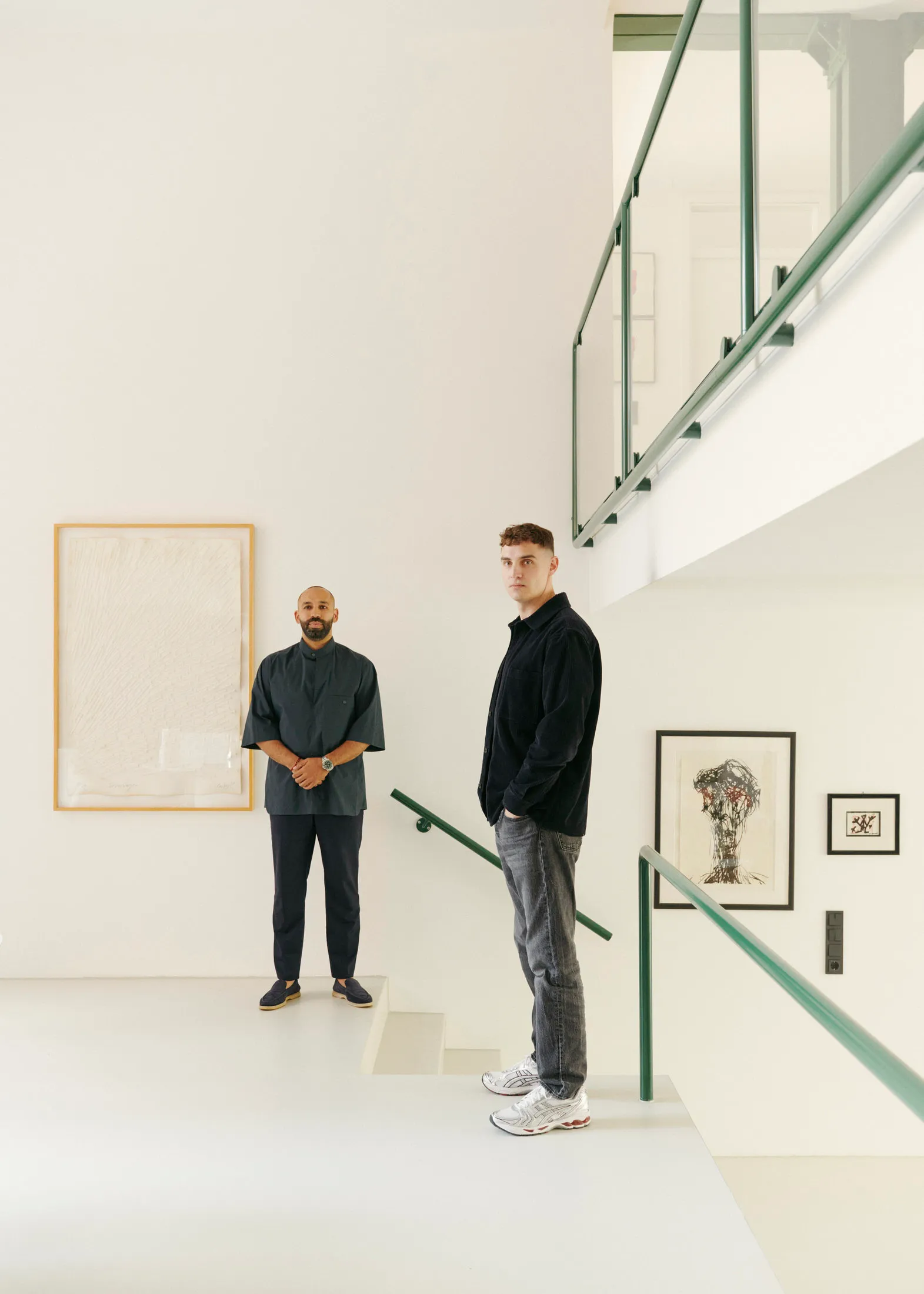 Two men standing in a modern art gallery with white walls and minimalist design.