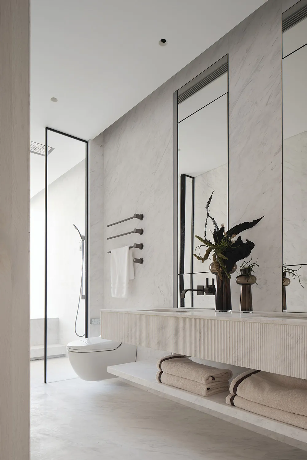 Modern bathroom interior featuring white marble walls and floor, a floating vanity, and a walk-in shower.