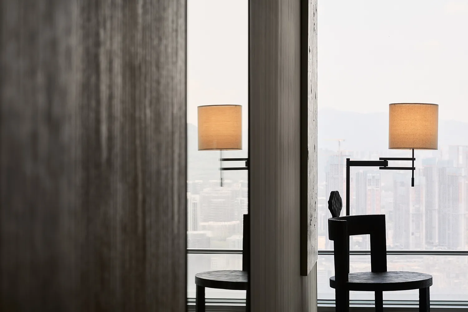 Modern minimalist office space featuring black wooden furniture and white lighting, with a view of a cityscape.
