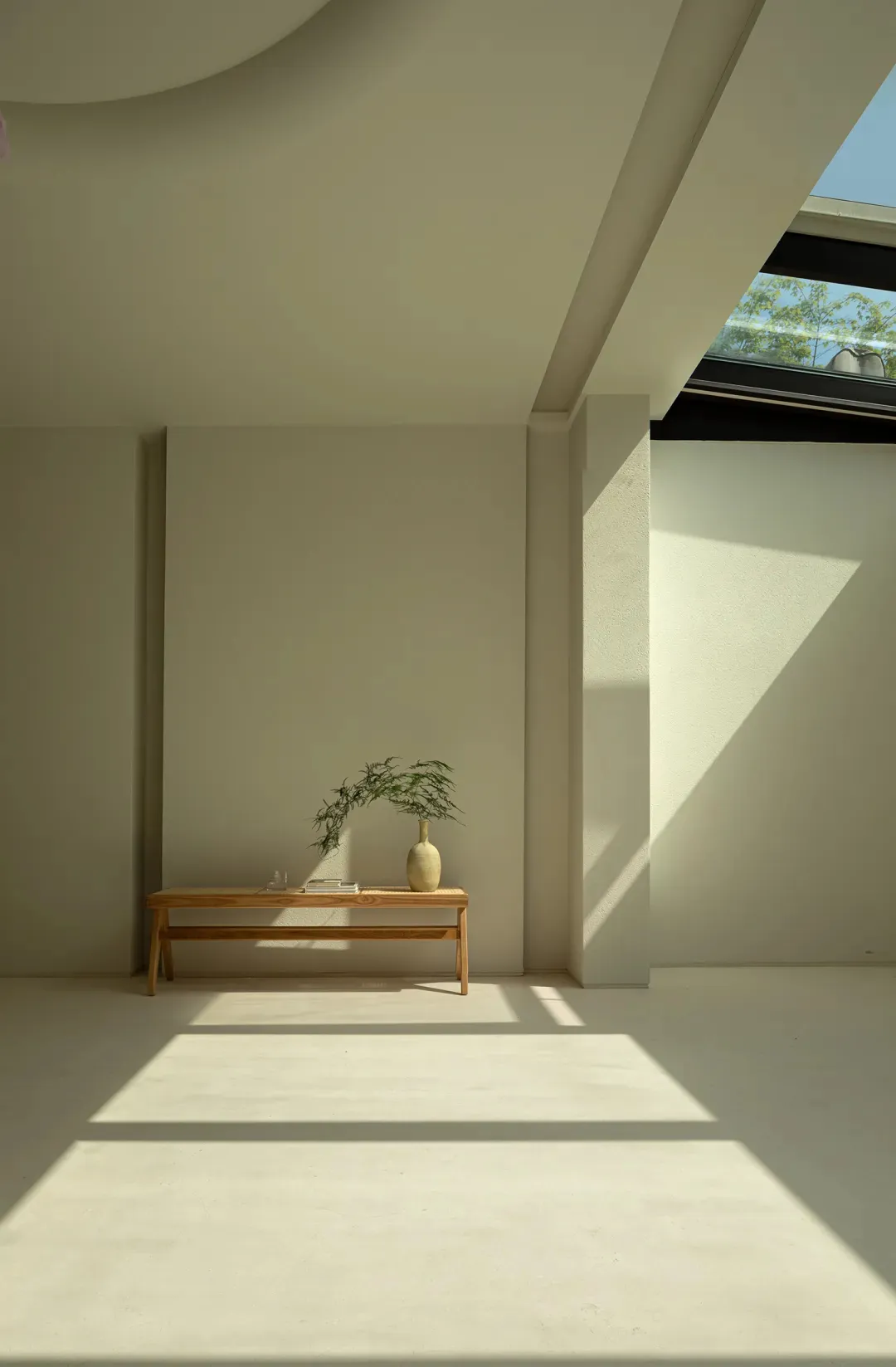 A minimalist interior space with concrete walls and floor, featuring a wooden bench adorned with a plant and a vase.